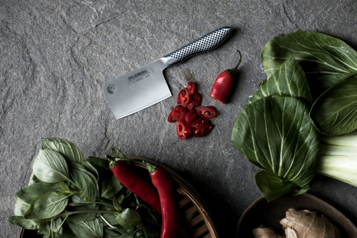 En liten kjøkkenkniv i stå, liggende ved siden av oppkuttet chili. Rund kanten av bildet ligger det hele røde chili og grønne salatbladergrønne salat blader
