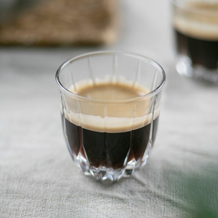 Et lite kaffeglass fylt med espresso plassert på et bord med duk på et