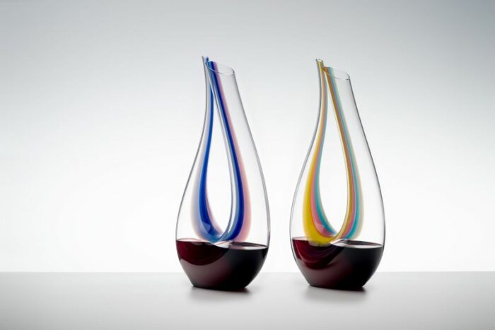 To vinkaraffel med skulpturell form i klart glass kombinert med farget glass. Begge karafflene er fylt med rødvin