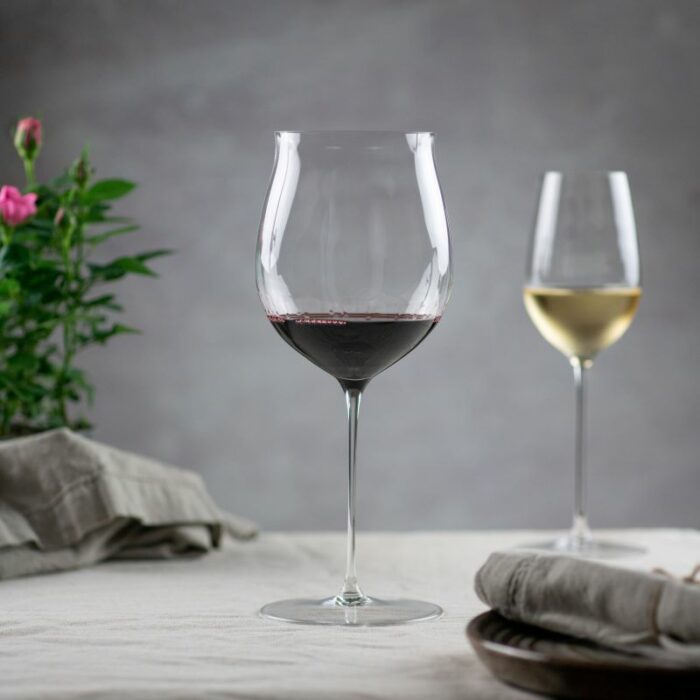 Et vinglass med rødvin og et vinglass med hvitvin ved siden av blomst og tøyserviett