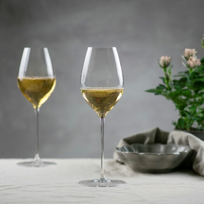 To vinglass med hvitvin ved siden av skål, blomst og tøyserviett