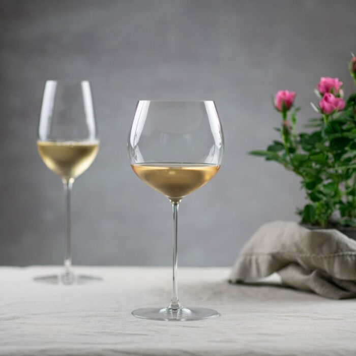 To ulike vinglass med hvitvin ved siden av blomst og tøyserviett